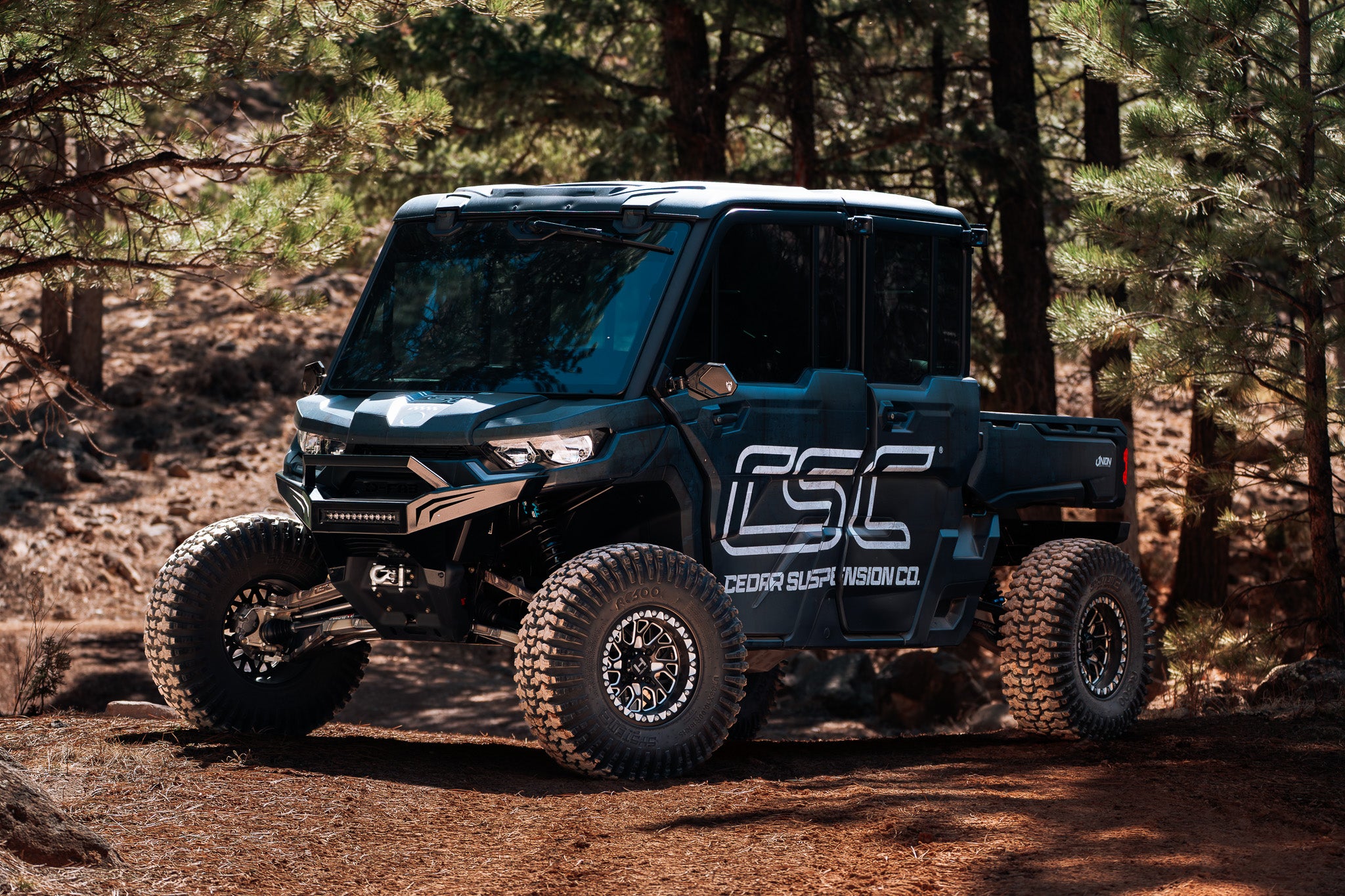 Blue off-road Can-Am Defender HD10 vehicle with CSC logo in a forest setting